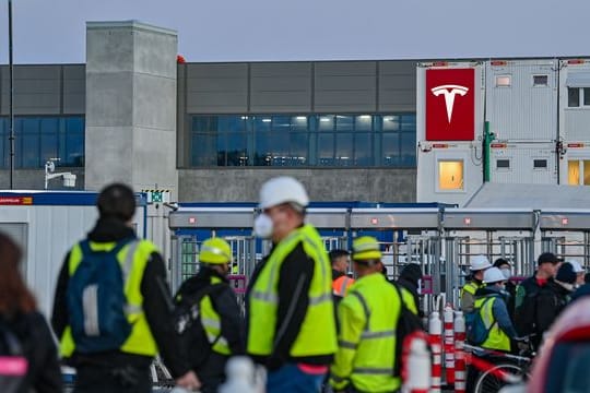 Arbeiter vor dem Tesla-Sitz in Grünheide: Der Fabrik fehlt noch eine Genehmigung für den Bau der Autos.