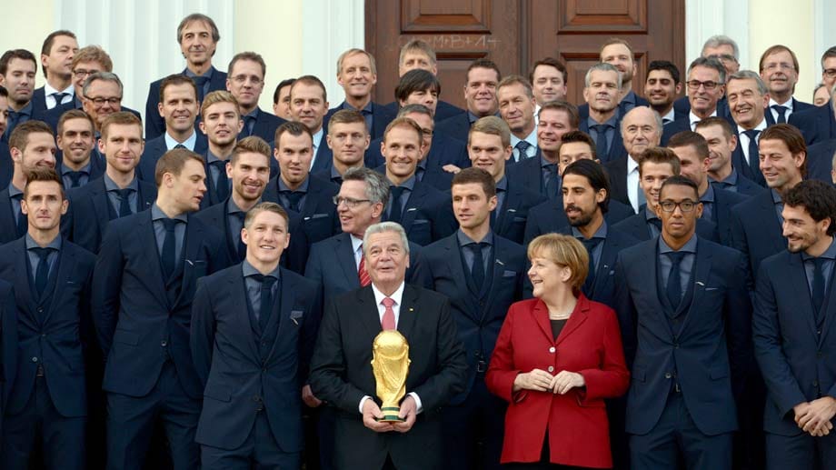 Zum Abschluss der Verleihung gibt es ein Gruppenfoto vor dem Schloss Bellevue. Joachim Gauck darf den WM-Pokal halten. Es scheint so, als würden sich die Kanzlerin und die Spieler darüber amüsieren, dass der Bundespräsident sein Glück offenbar kaum fassen kann. Vielleicht hat er aber auch nur Angst die Trophäe fallen zu lassen?