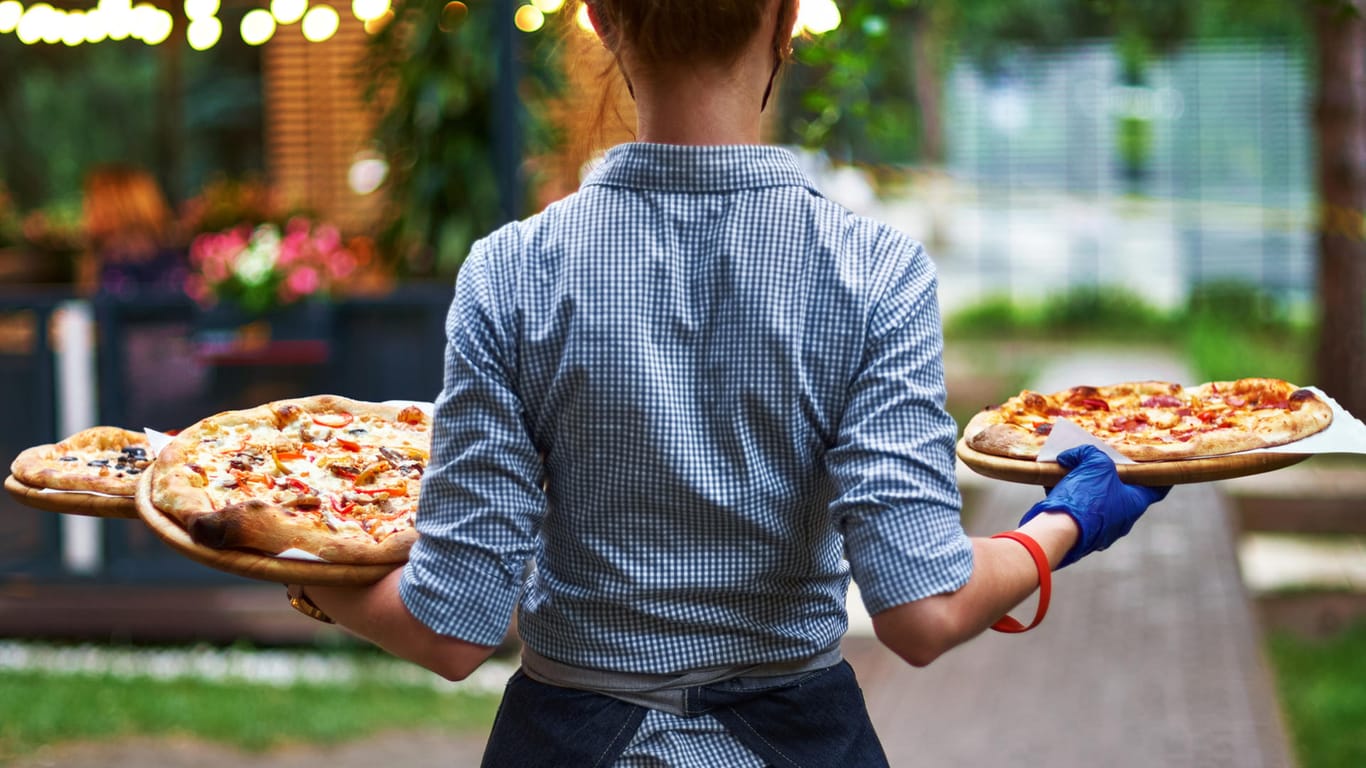 Eine Kellnerin bringt Gästen Pizza (Symbolbild): Wer den Mindestlohn bekommt, kann sich ab Januar über etwas mehr Einkommen freuen.