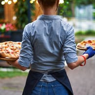 Eine Kellnerin bringt Gästen Pizza (Symbolbild): Wer den Mindestlohn bekommt, kann sich ab Januar über etwas mehr Einkommen freuen.