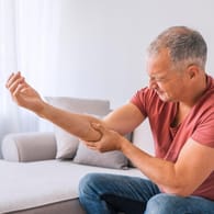 Ein Mann fasst sich wegen Schmerzen an seinen Unterarm: Fehlen dem Körper Mineralstoffe, wie Magnesium, Kalium oder Kalzium können Muskelschmerzen die Folge sein.