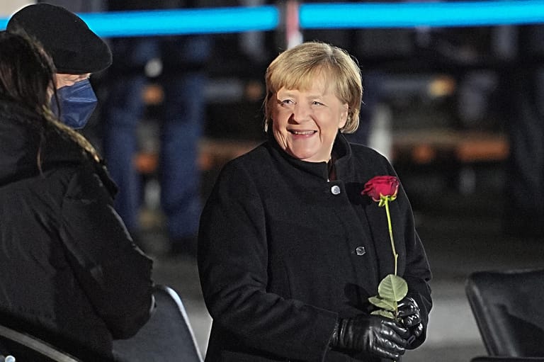 Angela Merkel: Zum Abschied nimmt sich die Kanzlerin noch eine Rose mit, die zahlreich für sie aufgestellt worden waren.