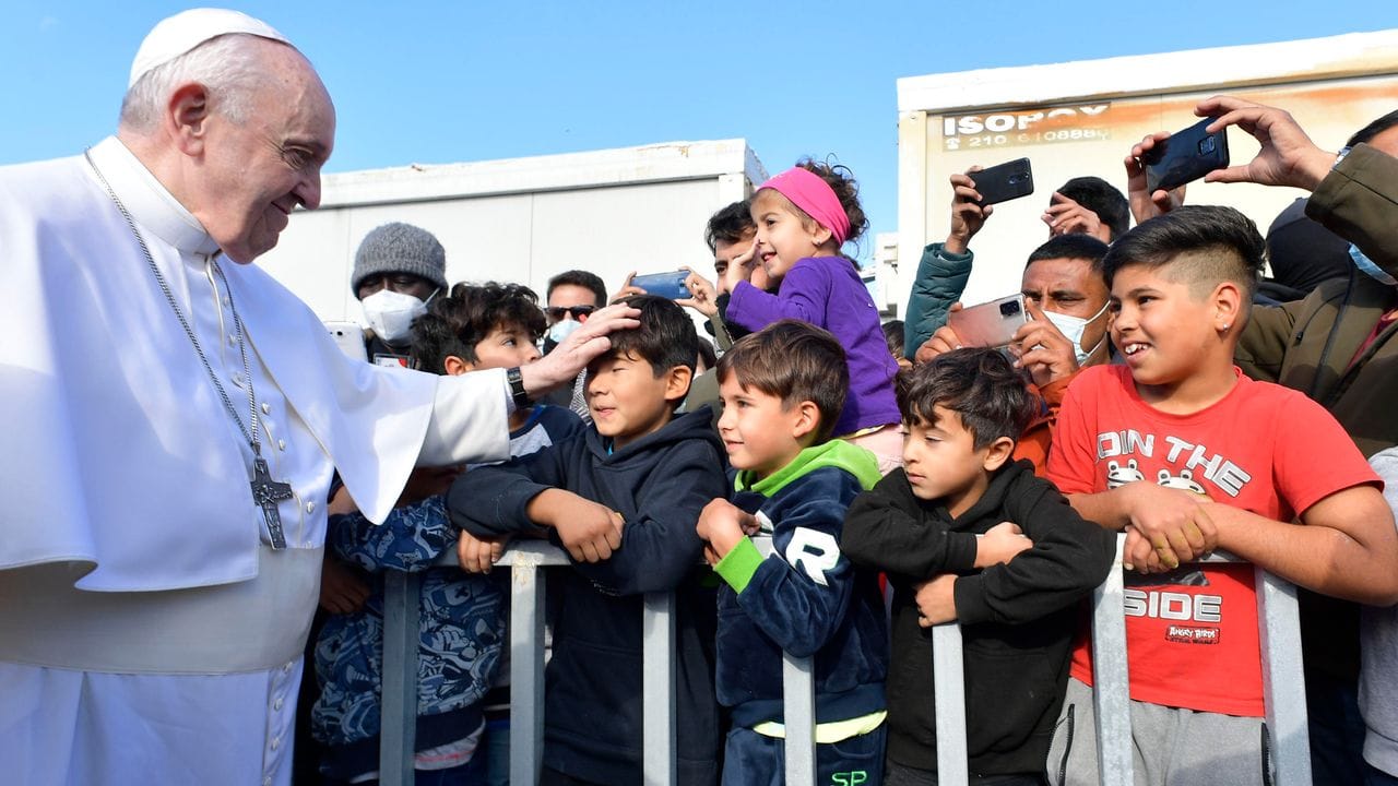 Papst Franziskus (l) legt einem Jungen im Flüchtlingslager auf der Insel Lesbos die Hand auf den Kopf.