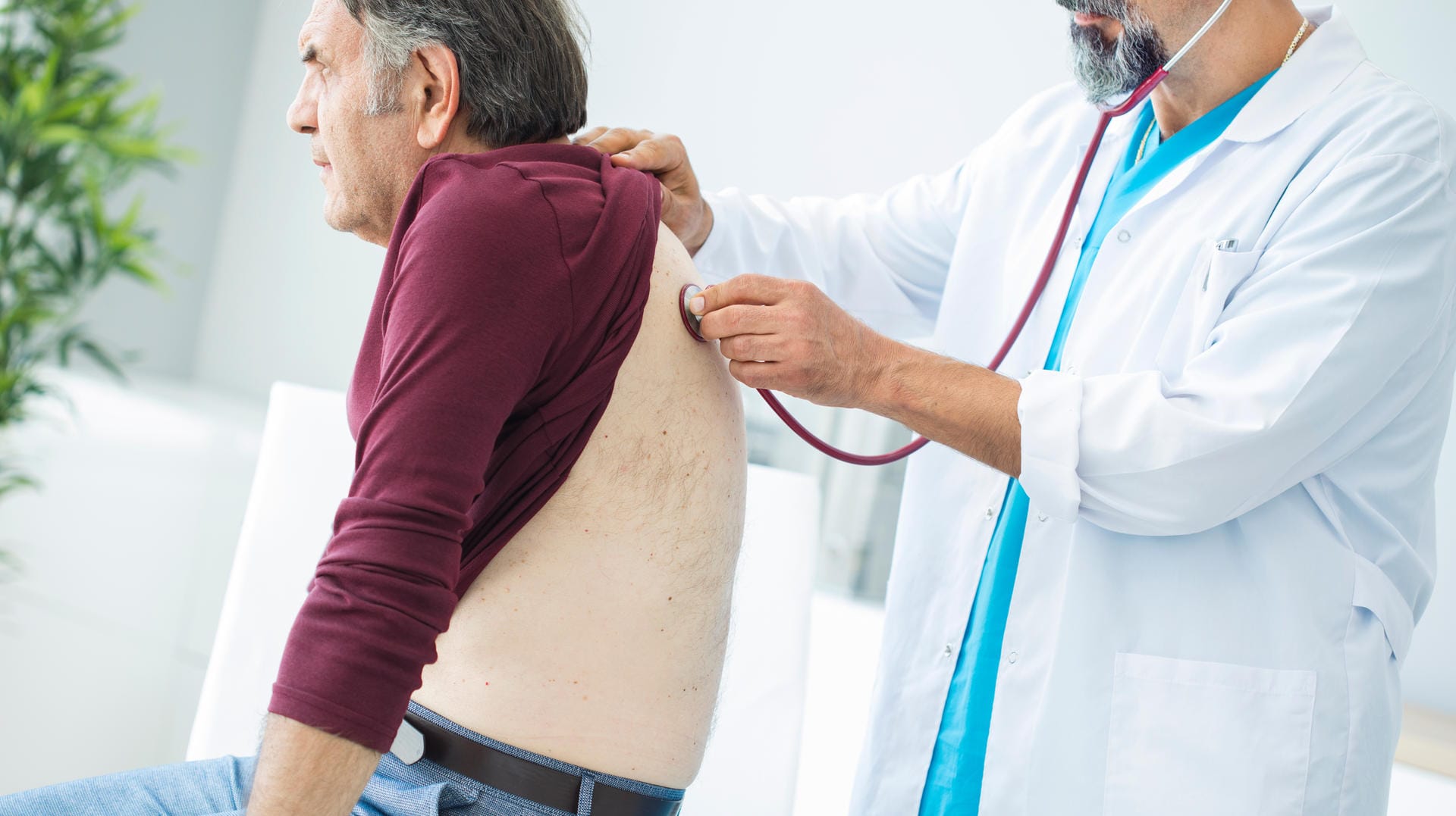 Ein Arzt hört bei einem Patienten die Lunge ab.