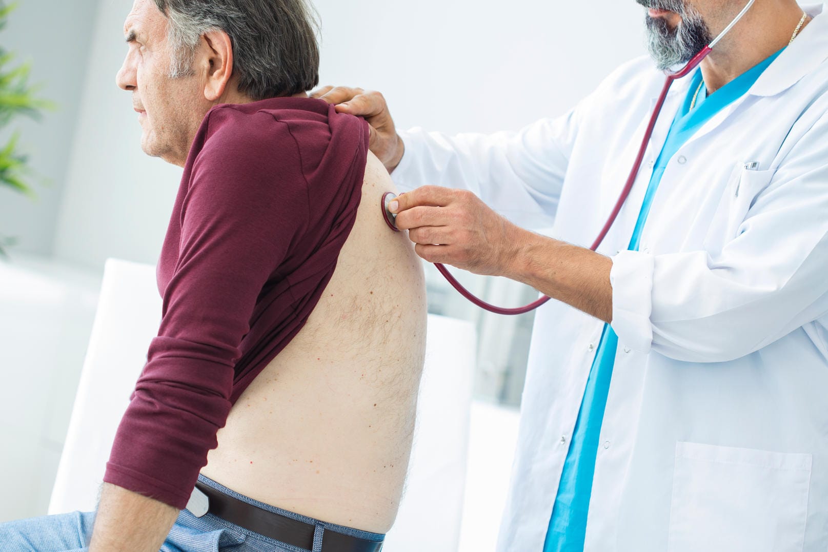 Ein Arzt hört bei einem Patienten die Lunge ab.