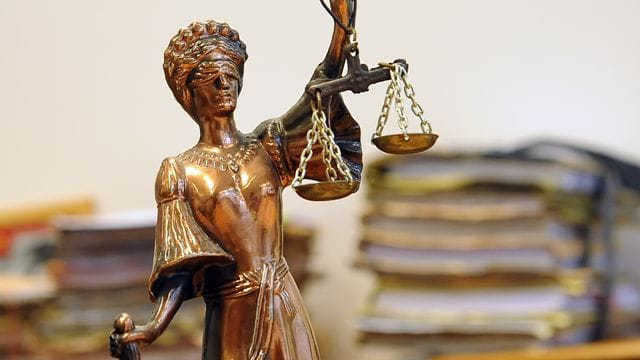 Eine goldfarbene Justitia-Figur steht vor Aktenbergen Eine goldfarbene Justitia-Figur steht vor Aktenbergen