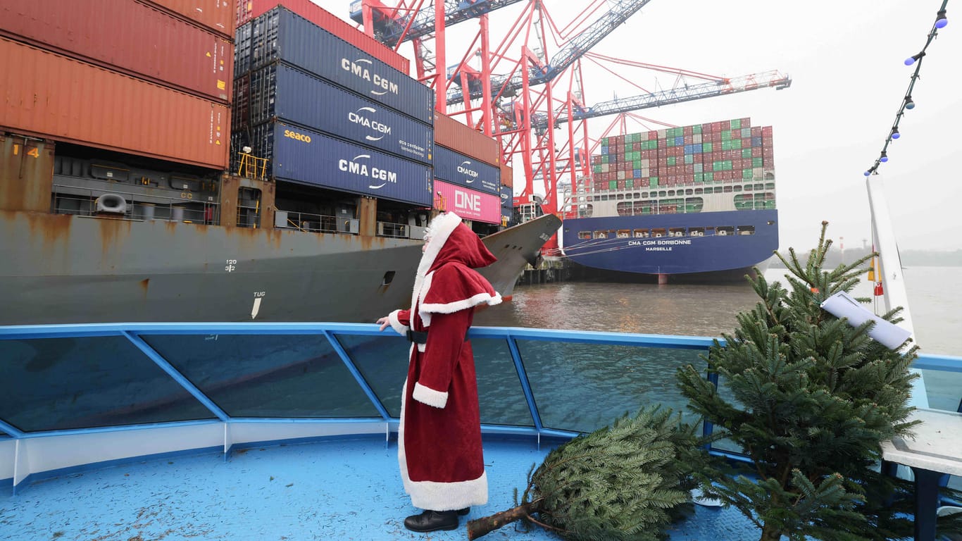 Ein Mann mit Weihnachtsmann-Kostüm steht an Bord eines Ausflugsschiffes im Hamburger Hafen: Er verteilt Weihnachtsbäume an die Besatzung der Frachtschiffe.