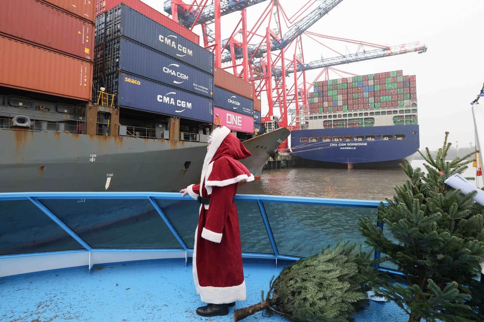 Ein Mann mit Weihnachtsmann-Kostüm steht an Bord eines Ausflugsschiffes im Hamburger Hafen: Er verteilt Weihnachtsbäume an die Besatzung der Frachtschiffe.