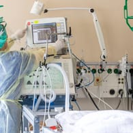 Eine Pflegekraft überprüft Instrumente am Bett eine Corona-Patienten (Archivbild): Noch immer sind die Infektionszahlen fünfstellig.