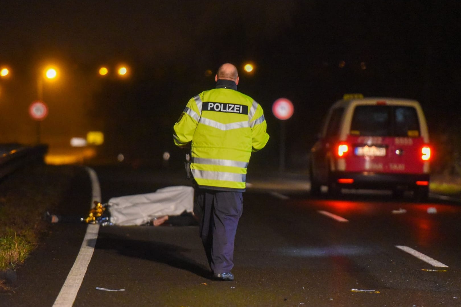 Ein Polizist am Unfallort, im Hintergrund sind das Taxi und das Opfer zu sehen: Der Mann wurde so schwer verletzt, das er noch am Unfallort verstarb.