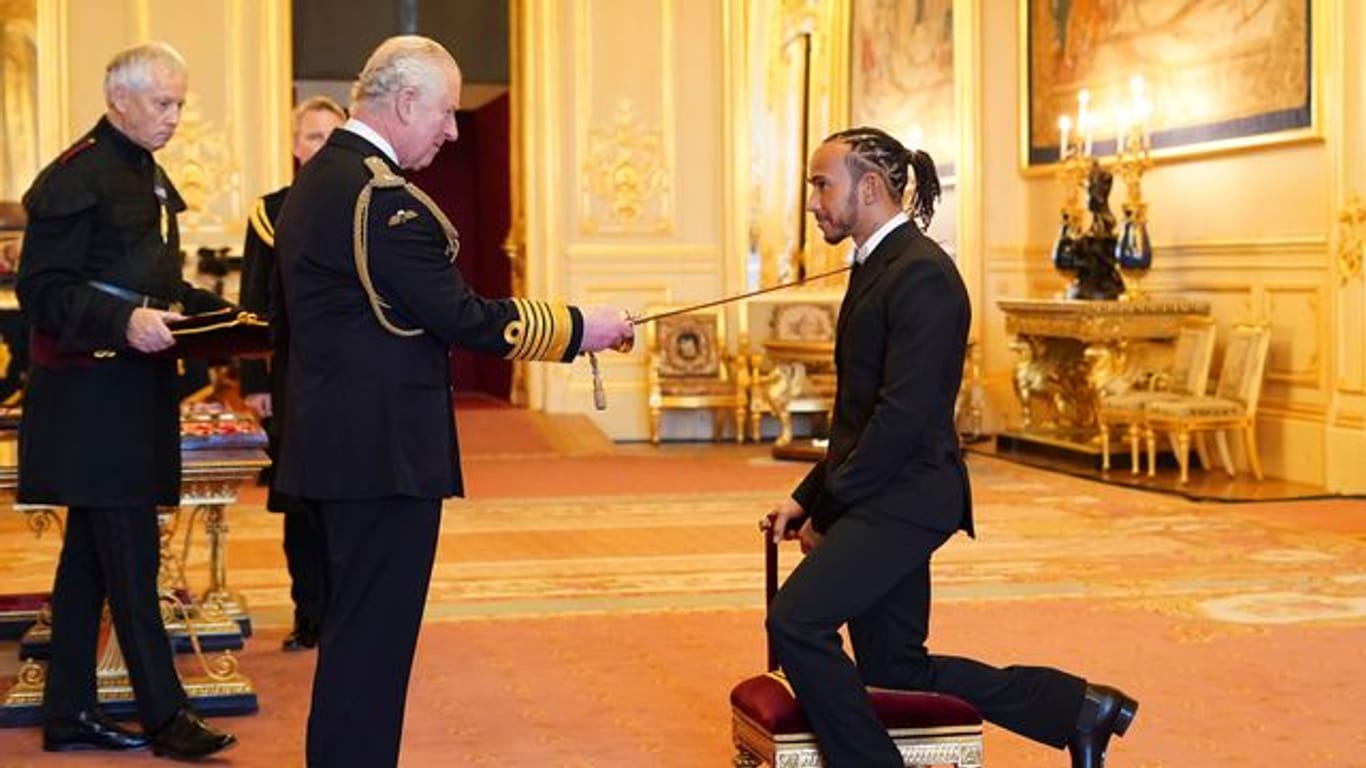 Prinz Charles schlägt Lewis Hamilton (r) auf Schloss Windsor zum Ritter.