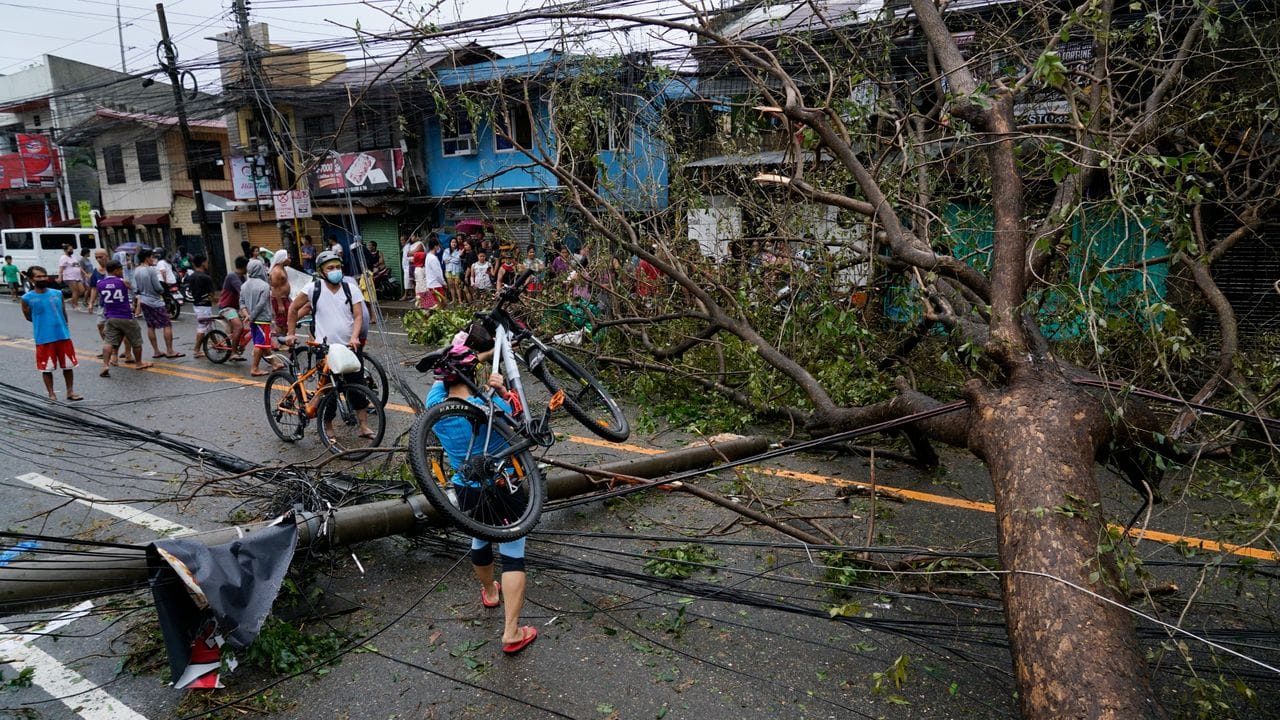 Ein Anwohner trägt ein Fahrrad über einen umgestürzten Strommast und einen Baum. Ein Anwohner trägt ein Fahrrad über einen umgestürzten Strommast und einen Baum.