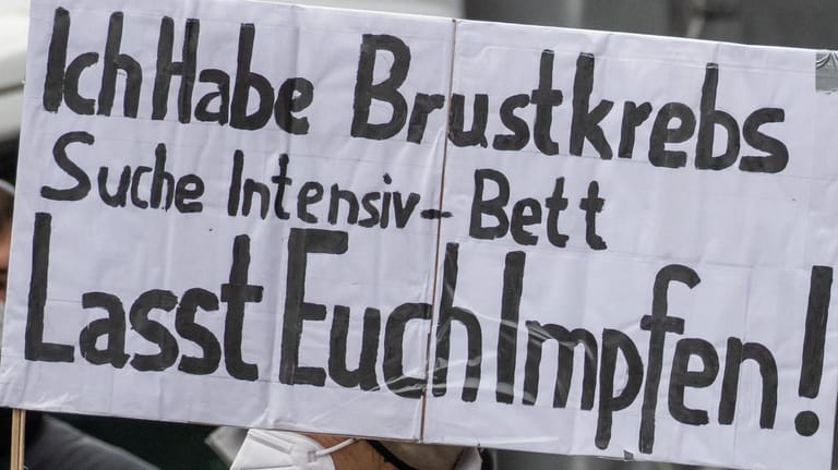 Eine Gegendemonstrantin hält ein Plakat mit der Aufschrift "Ich habe Brustkrebs. Suche Intensiv-Bett. Lasst euch Impfen!": In mehreren Kommunen war es zu Gegenprotesten gekommen.