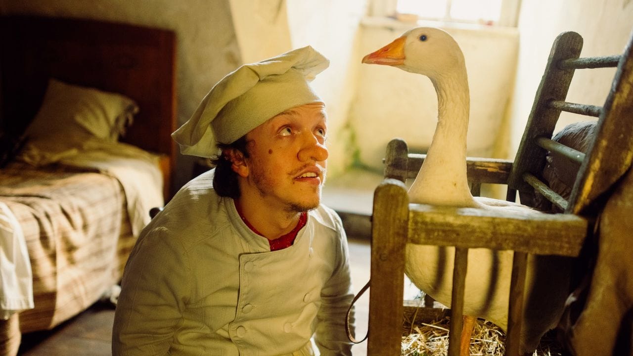 Inmitten seiner ärmlichen Kammer kniet Zwerg Nase (Mick Mehnert) vor einem Holzkäfig, aus dem die Gans Mimi hinausschaut. Inmitten seiner ärmlichen Kammer kniet Zwerg Nase (Mick Mehnert) vor einem Holzkäfig, aus dem die Gans Mimi hinausschaut.