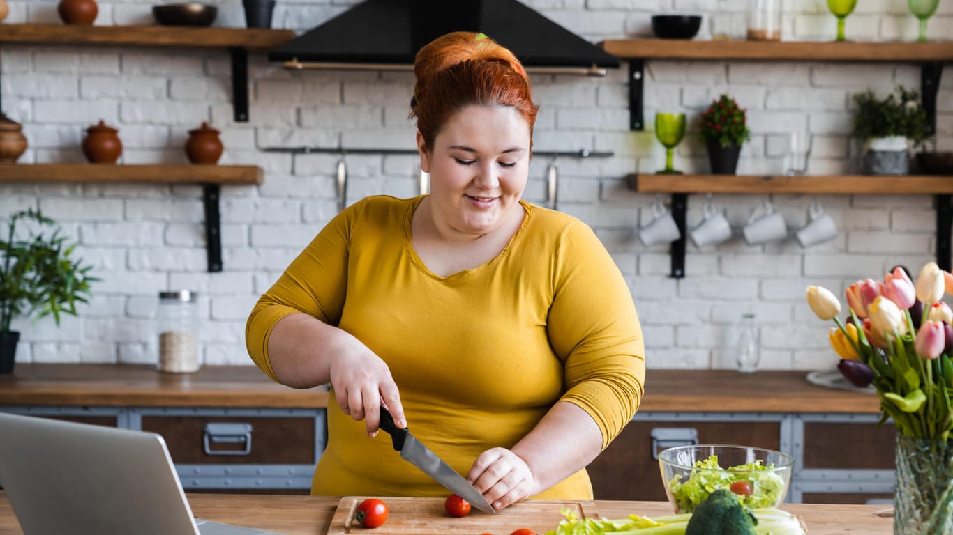 Eine übergewichtige Frau beim Kochen. Eine gesunde Ernährung ist für Menschen mit Diabetes mellitus ein wichtiger Therapiebaustein.