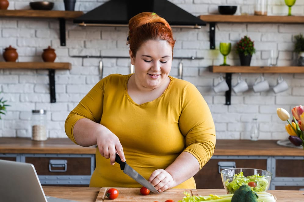 Eine übergewichtige Frau beim Kochen. Eine gesunde Ernährung ist für Menschen mit Diabetes mellitus ein wichtiger Therapiebaustein.
