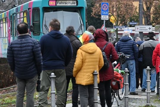 Impfwillige stehen an der Wendeschleife am Frankfurter Zoo vor einer zum Impf-Express umgerüsteten Straßenbahn: Bis zum 30. Dezember werden Impftermine in der Bahn angeboten.