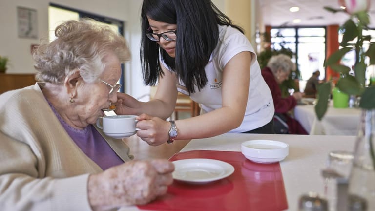 Die Altenpflegerin Song Xi aus China hilft einer Seniorin beim Essen: Zuwanderer sollen den Notstand beim Personal lindern, fordert die Kommunen. (Archivbild)