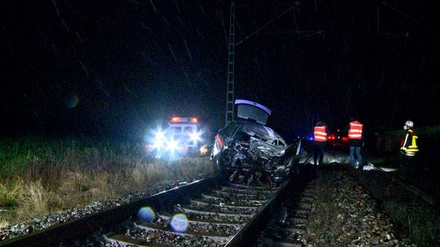 Einsatzkräfte neben dem beschädigten Auto: Ein Zug schleifte den Wagen mit. Einsatzkräfte neben dem beschädigten Auto: Ein Zug schleifte den Wagen mit.