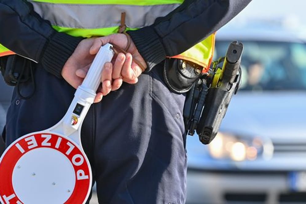 Ein Polizeibeamter hält eine Winkerkelle in den Händen (Symbolbild): Der Fahrer konnte keinen Führerschein vorweisen.