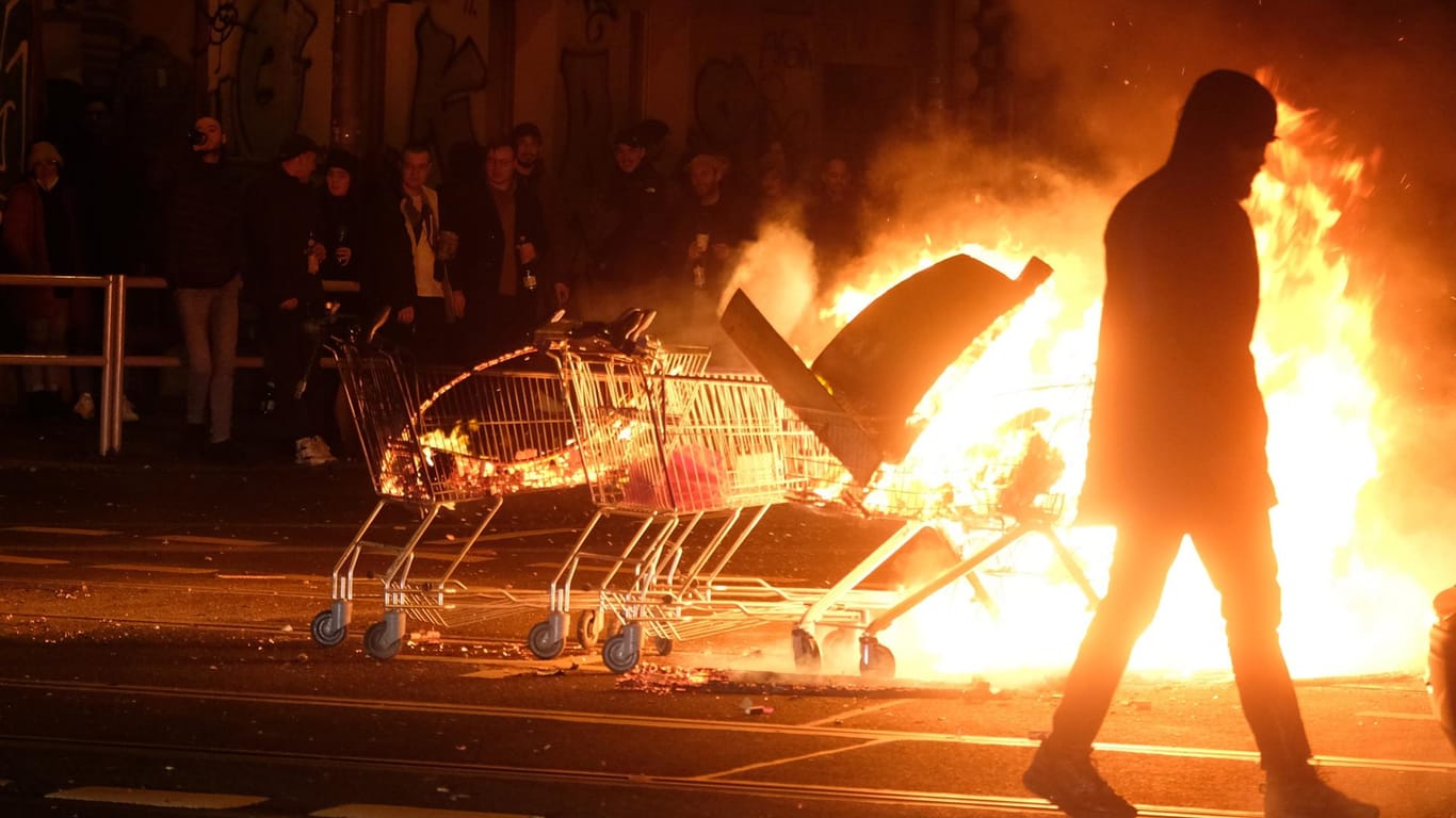 Ein Mann geht an der Eisenbahnstraße an Einkaufswagen mit brennenden Gegenständen: Im Leipziger Osten ist es in der Neujahrsnacht zu Ausschreitungen gekommen.
