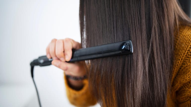 Frau benutzten Glätteisen: Zu viel Hitze schadet dem Haar. Bei regelmäßigen Haareglätten trocknen die Haare aus und brechen leichter ab.