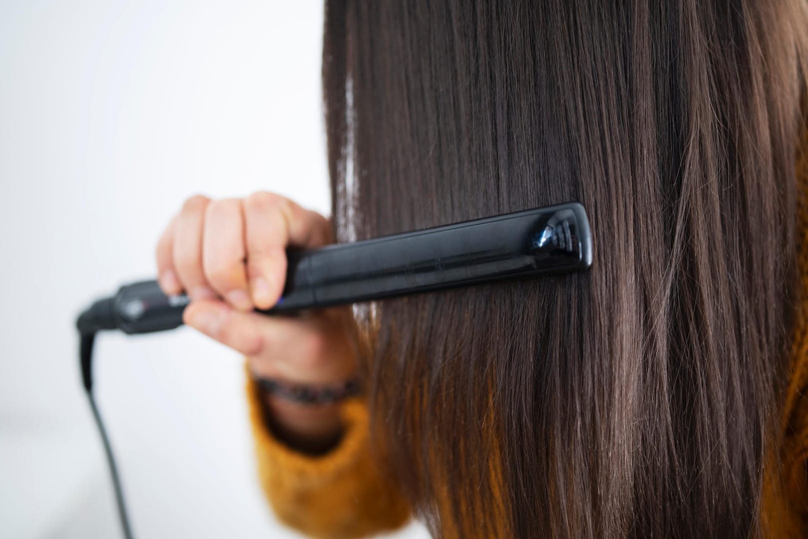 Frau benutzten Glätteisen: Zu viel Hitze schadet dem Haar. Bei regelmäßigen Haareglätten trocknen die Haare aus und brechen leichter ab.