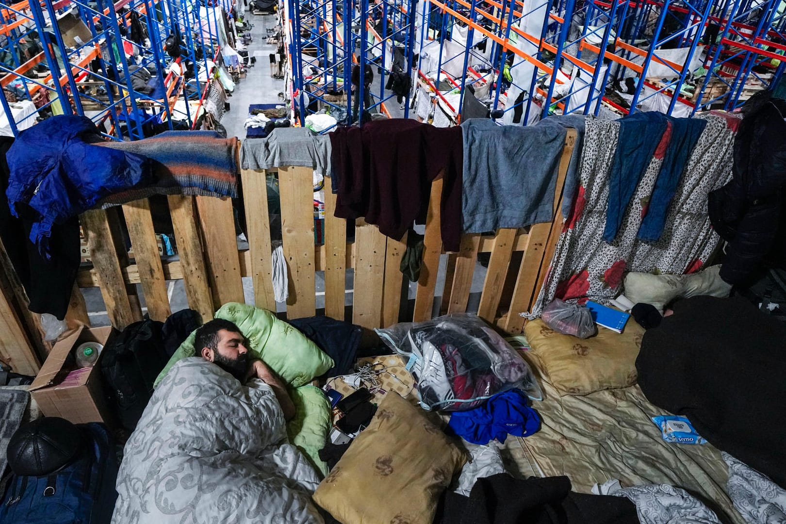 Ein Mann schläft in einem Logistikzentrum an der belarussisch-polnischen Grenze: Auch im neuen Jahr harren weiter hunderte Migranten an der Grenze aus.