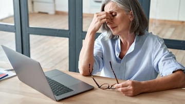 Überarbeitete ältere Frau sitzt am Tisch und fasst sich ins Gesicht: Stress ist die häufigste Ursache für Schlafstörungen. Das ständige Nachdenken über private oder berufliche Probleme hält viele vom Ein- oder Durchschlafen ab.