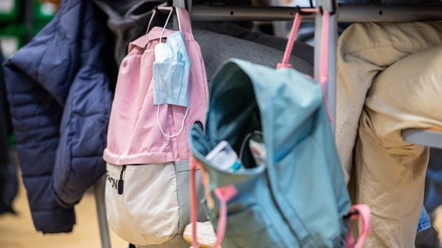 Masken hängen in einem Klassenzimmer an Rucksäcken von Schülern Masken hängen in einem Klassenzimmer an Rucksäcken von Schülern
