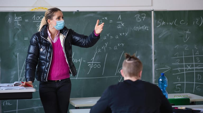 Lehrerin mit dicker Winterjacke und Mund-Nasen-Schutz im Unterricht (Symbolbild): Schüler müssen sich jetzt warm anziehen – am Montag starten NRWs Schulen im Präsenzmodus.
