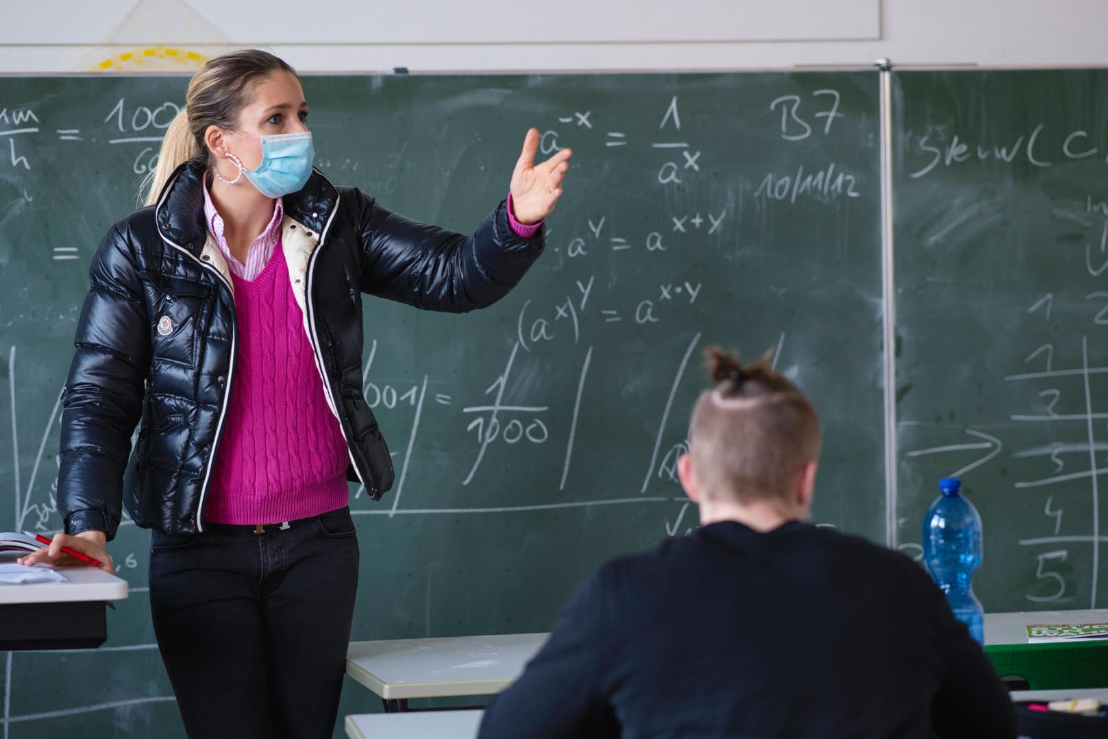 Lehrerin mit dicker Winterjacke und Mund-Nasen-Schutz im Unterricht (Symbolbild): Schüler müssen sich jetzt warm anziehen – am Montag starten NRWs Schulen im Präsenzmodus.