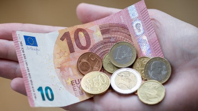 Eine Frau hält einen 10-Euro-Schein und Münzen in der Hand