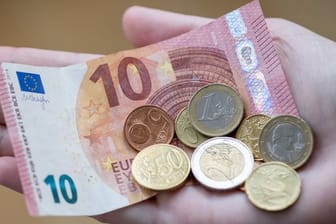 Eine Frau hält einen 10-Euro-Schein und Münzen in der Hand