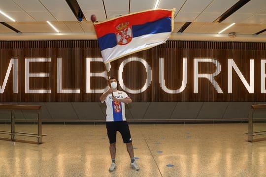Ein Fan von Novak Djokovic schwenkt in der Ankunftshalle des Flughafens Melbourne eine serbische Fahne.