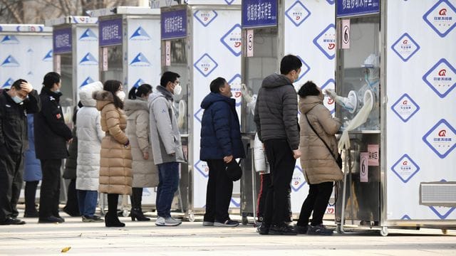 Menschen warten im Pekinger Stadtbezirk Xicheng im Rahmen eines Corona-Massentests vor Test-Kabinen.