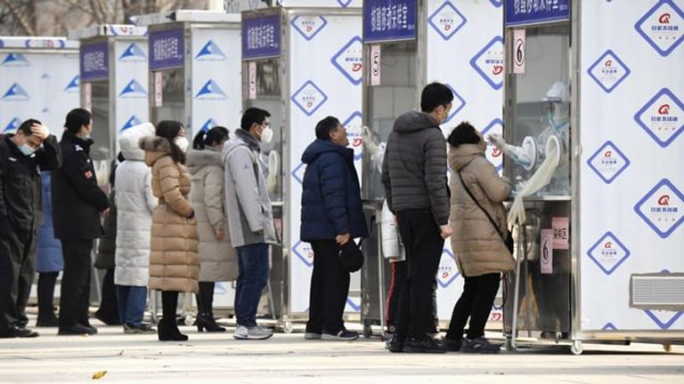Menschen warten im Pekinger Stadtbezirk Xicheng im Rahmen eines Corona-Massentests vor Test-Kabinen.