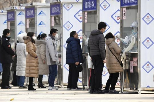 Menschen warten im Pekinger Stadtbezirk Xicheng im Rahmen eines Corona-Massentests vor Test-Kabinen.