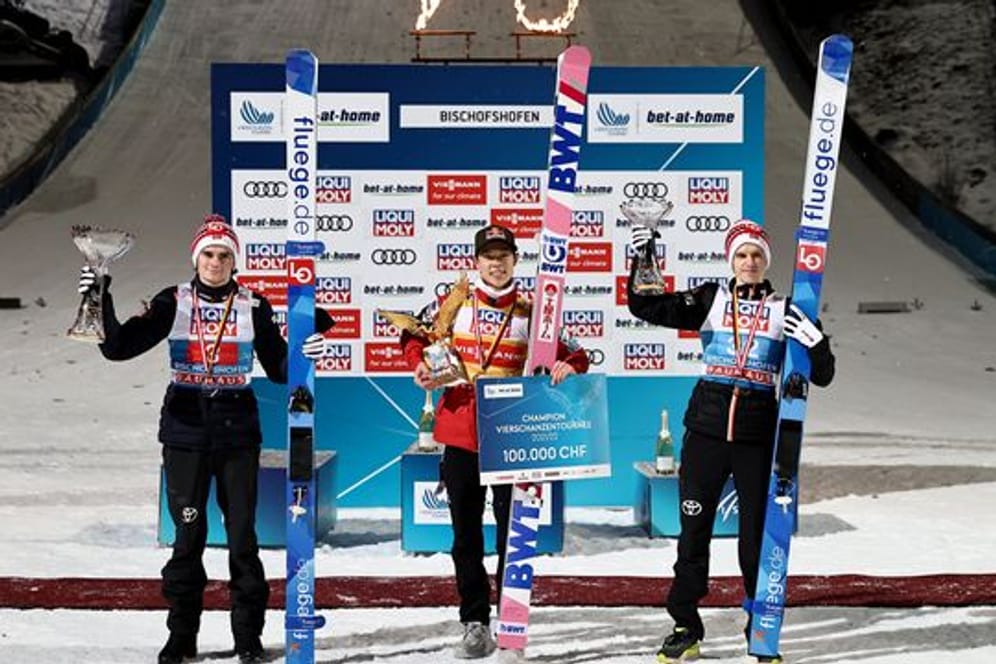Ryoyu Kobayashi (M) jubelt mit dem Pokal für den Gesamtsieger, einem goldenen Adler, neben dem Gesamtzweiten Marius Lindvik (l) und dem Gesamtdritten Halvor Egner Granerud.