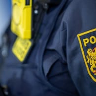 Eine Polizistin trägt ein Abzeichen der bayerischen Polizei (Symbolbild): Durch einen Spalt beschmutzte ein Mann zwei Beamte.
