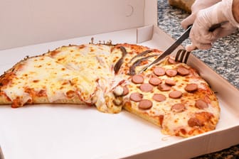 Eine Pizza wird geschnitten (Symbolbild): Ein Pizzabote wurde bei einer Lieferung überfallen.