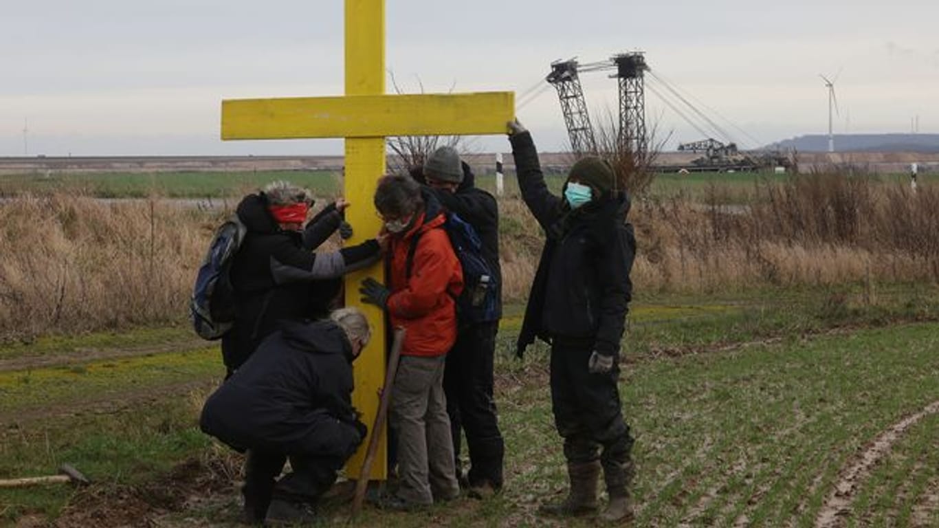 Demonstranten stellen am Rande des Braunkohletagebaus bei Lützerath ein gelbes Kreuz auf.