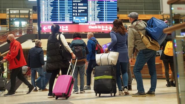 Reisende stehen am Flughafen BER vor einer Info-Tafel.