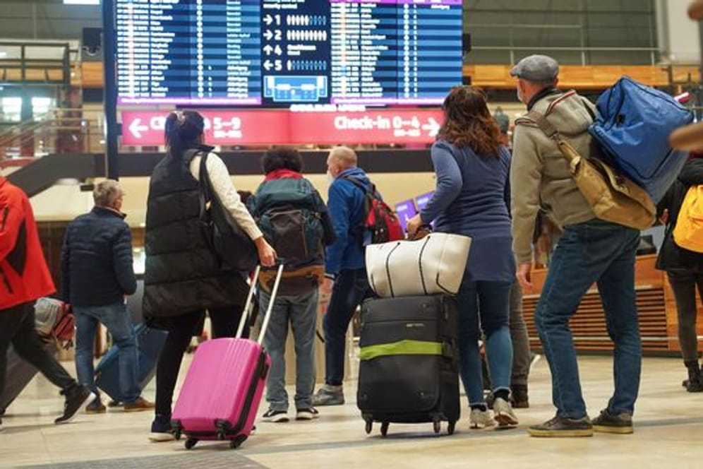 Reisende stehen am Flughafen BER vor einer Info-Tafel.