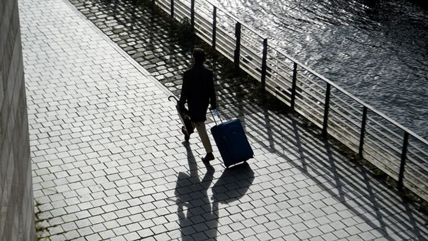 Ein Mann geht mit seinem Koffer am Spreeufer entlang