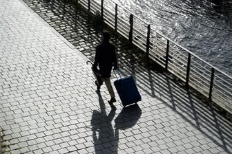 Ein Mann geht mit seinem Koffer am Spreeufer entlang