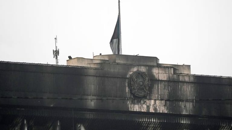 Die Nationalflagge auf halbmast und das Staatswappen von Kasachstan auf der verrußten Fassage des Rathausgebäudes in Almaty.