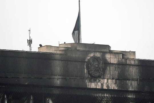 Die Nationalflagge auf halbmast und das Staatswappen von Kasachstan auf der verrußten Fassage des Rathausgebäudes in Almaty.