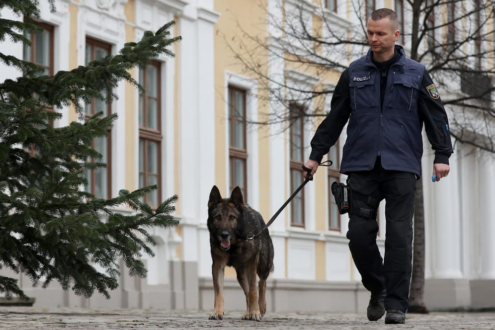 Polizist untersucht mit einem Sprengstoffspürhund den Außenbereich des Landtags in Magdeburg: Gegen den anonymen Absender der Drohung wird ermittelt.