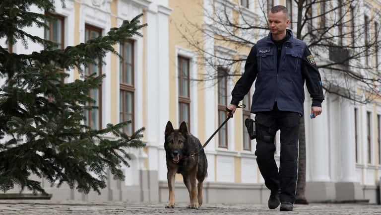Polizist untersucht mit einem Sprengstoffspürhund den Außenbereich des Landtags in Magdeburg: Gegen den anonymen Absender der Drohung wird ermittelt.